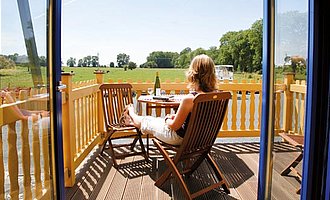 Blick über den Balkon einer Ferienwohnung im Elsass. Auf dem Balkon sitzt eine Frau die in die Ferne schaut und ein Glas Wein trink.