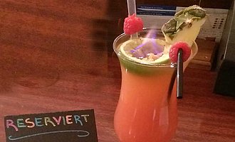 Cocktailglas mit rötlichem Drink, garniert mit Himbeeren und Ananas